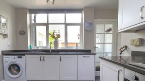 Una cucina moderna con mobili bianchi, una lavatrice integrata, un'ampia finestra con vista e un orologio appeso al muro.