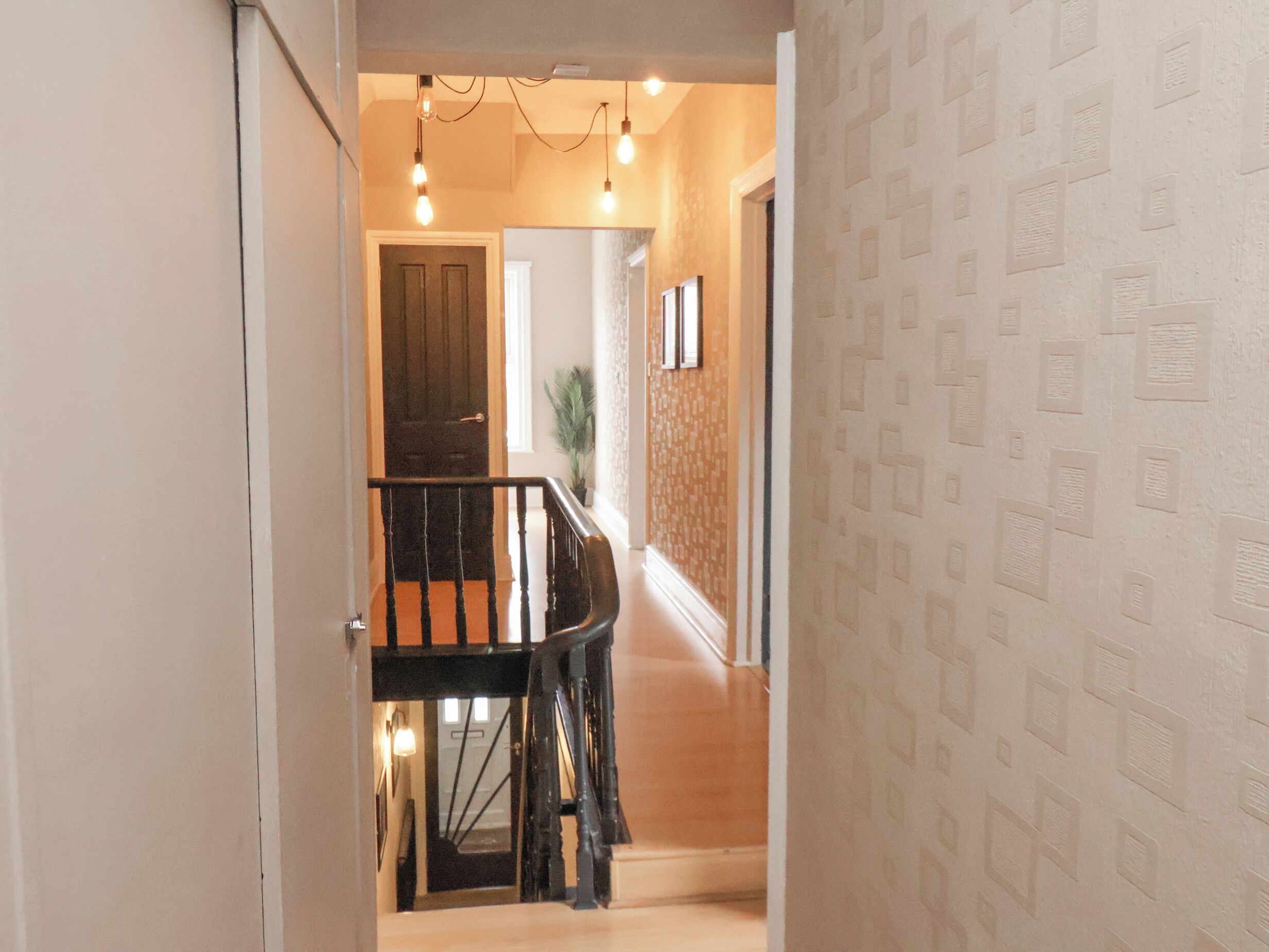 A hallway with a wooden staircase, a door at the end, and a patterned wall.