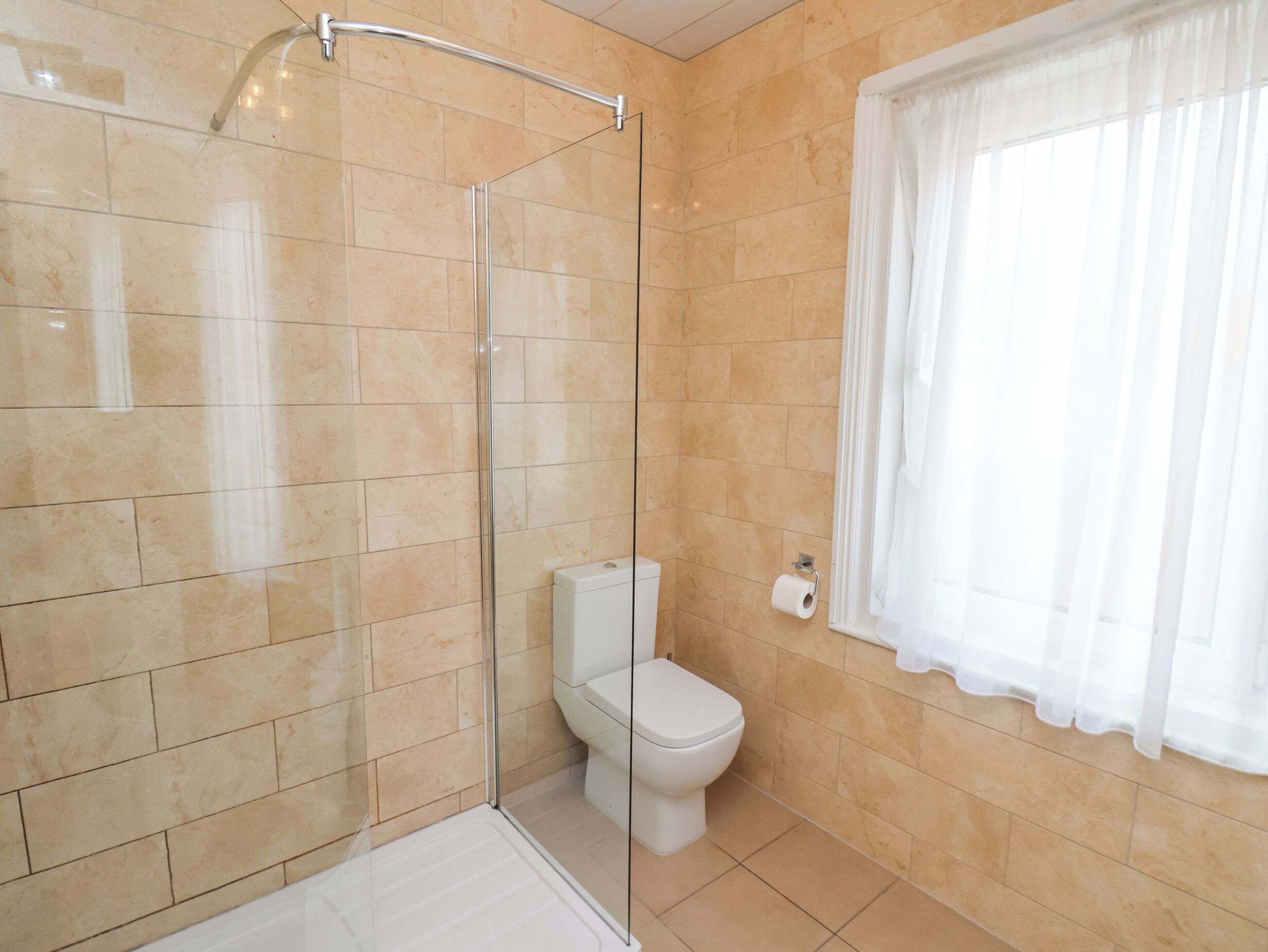 Un bagno con doccia vetrata, un water e una finestra con tende bianche.