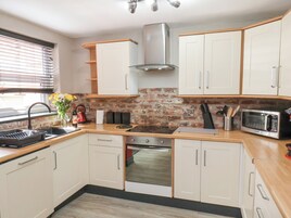 A kitchen with white cabinets, a brick backsplash, a stainless steel range hood, a microwave, and a sink with a faucet.
