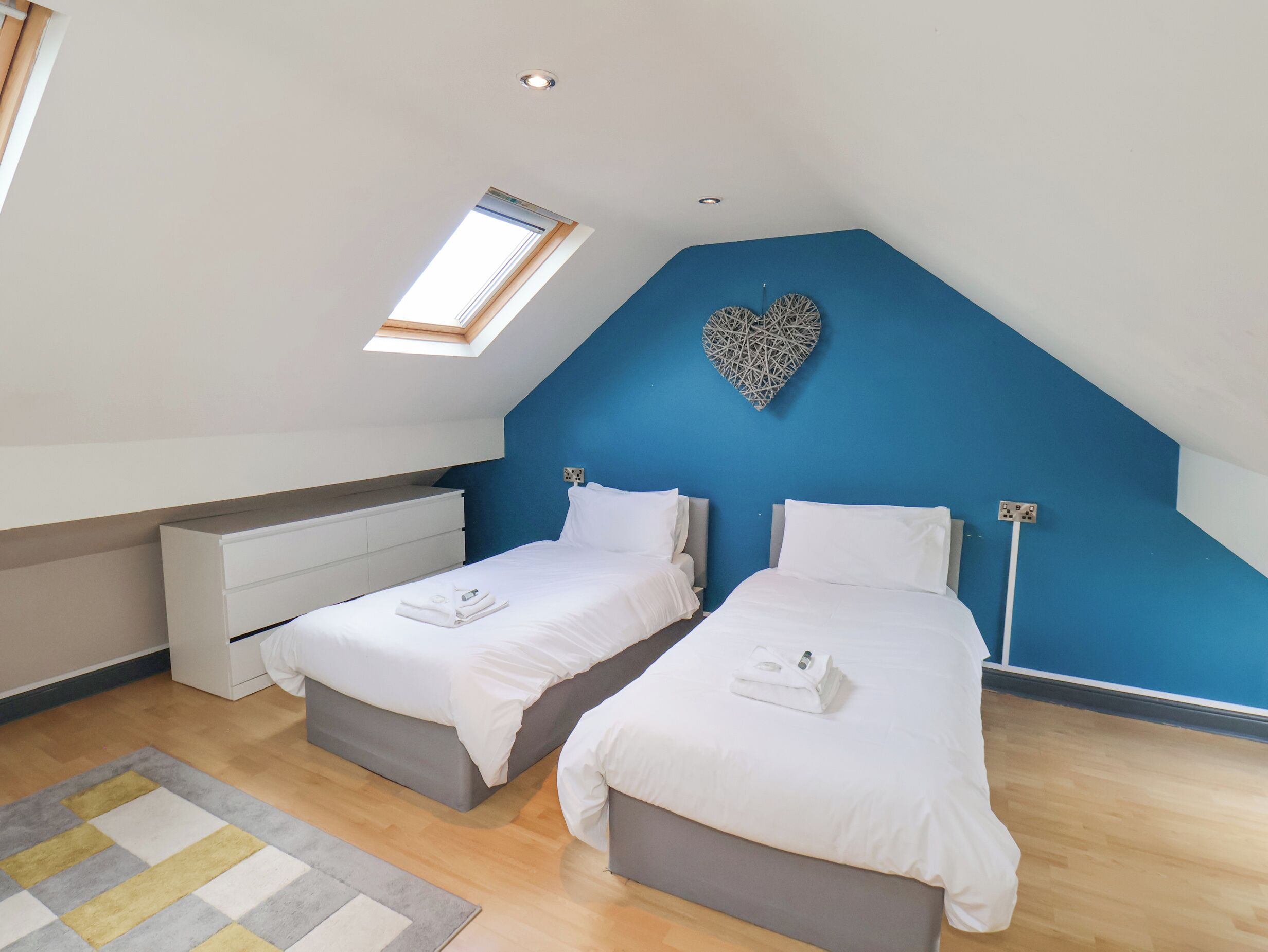 Une chambre avec deux lits, une lucarne, un élément de décoration murale en forme de cœur et une table de chevet.