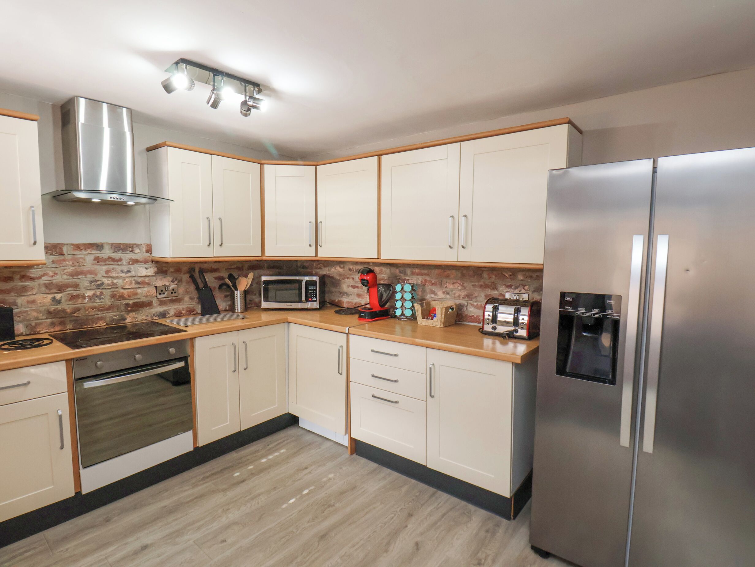 A modern kitchen with white cabinets, a stainless steel refrigerator, a microwave, a toaster, and a gas stove.