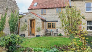 Une maison en pierre avec un toit recouvert de tuiles rouges, un petit jardin et une porte en bois.