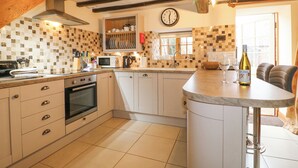 Une cuisine avec des meubles blancs, un four à micro-ondes, une cuisinière et une horloge au mur.