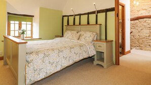 Une chambre à coucher avec un lit, des tables de chevet, une fenêtre et un mur en pierre.