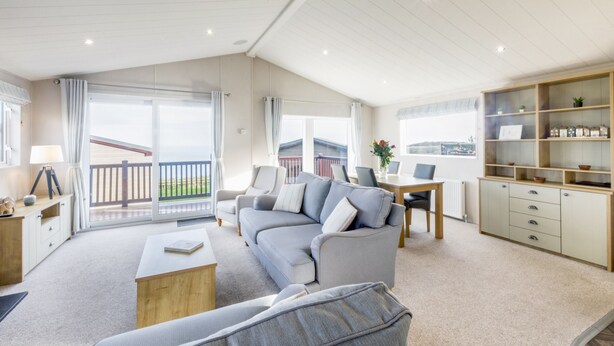 A spacious living room with a grey sofa, a wooden coffee table, and a dining area with a table and chairs. - Lodge 58 at Riviera Bay Coastal Retreat (Brixham)