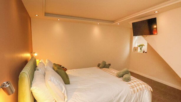 A bedroom with a large bed, a flat-screen TV mounted on the wall, and a small window with blinds. - Picadore Two (Scarborough)