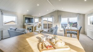 Un vaste espace de vie comprenant une table à manger en bois, un canapé et un téléviseur. Il y a des fenêtres avec des rideaux, une cheminée et une vue sur l’extérieur.