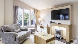 Un salon avec un canapé gris, une table basse en bois, une cheminée et un téléviseur fixé au mur.
