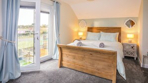 Een slaapkamer met een houten bed, twee nachtkastjes met lampen, een groot raam met gordijnen en uitzicht op de omgeving.