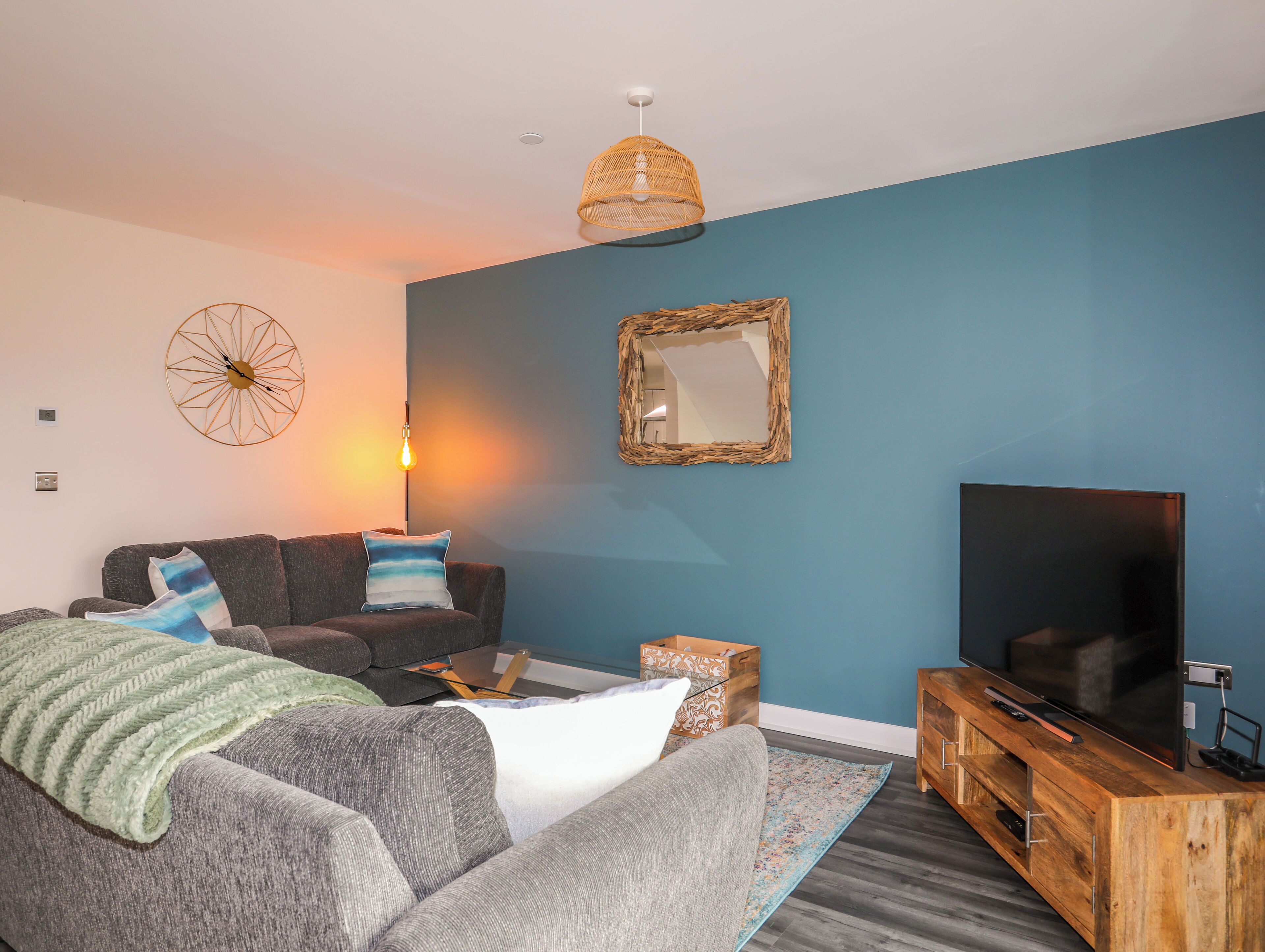A modern living room with a grey sofa, a coffee table, a TV, and a blue accent wall.