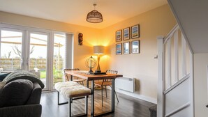 Een eethoek met een houten tafel, stoelen en een lamp. Op de voorgrond staat een bank en een sofa.
