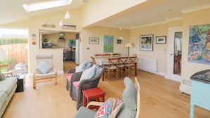 A spacious living area with a high ceiling, a dining table, wicker furniture, and a view of the kitchen. - Tree Tops (Newport)