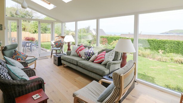 A spacious living room with a large window, a sofa set, and a dining area. - Tree Tops (Newport)