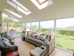 A spacious living room with a large window, a sofa set, and a dining area. - Tree Tops (Newport)