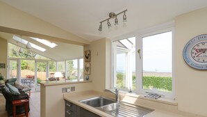 A kitchen with a large window, a sink, and a dining area with chairs and a table. - Tree Tops (Newport)