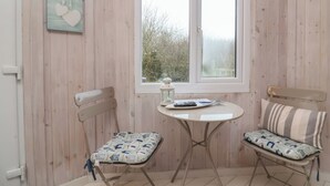 Une pièce chaleureuse aux murs en bois, une fenêtre offrant une belle vue, deux fauteuils avec des coussins à motifs, une petite table et un luminaire fixé au mur.