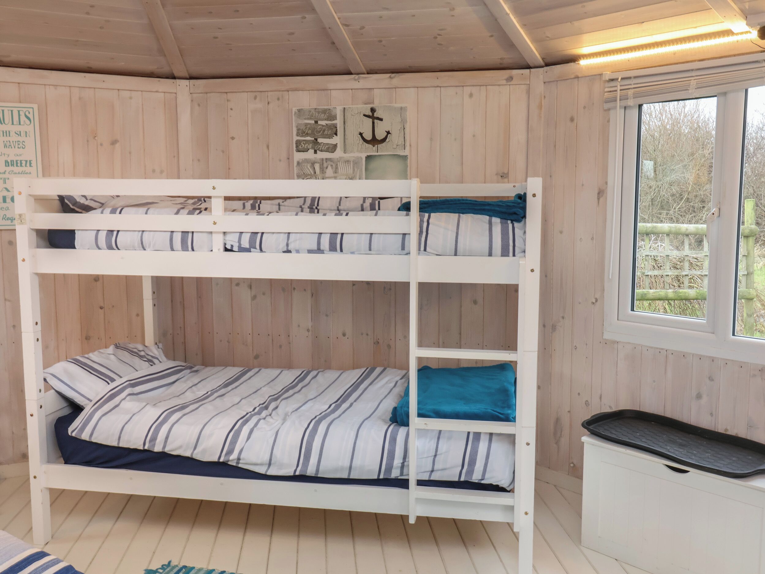 A bunk bed room with wooden walls, a window, and a small desk.