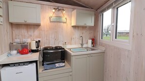 Une cuisine compacte aux murs en bois, dotée d’un four encastré, d’un évier et d’une fenêtre donnant sur l’extérieur.
