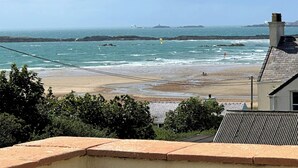 A coastal view with a beach, rocky outcrops, and a distant island. - Swyn Llyr (Rhosneigr)