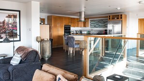 A modern kitchen with wooden cabinets, stainless steel appliances, and a glass staircase leading to an upper level. - Swyn Llyr (Rhosneigr)
