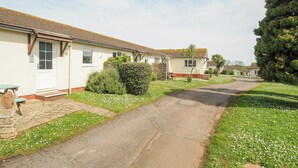 Une rangée de maisons de plain-pied, avec une allée pavée et une pelouse agrémentée de fleurs blanches.