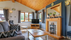 A cozy living room with a wooden ceiling, a sofa, a coffee table, a TV, and a fireplace.