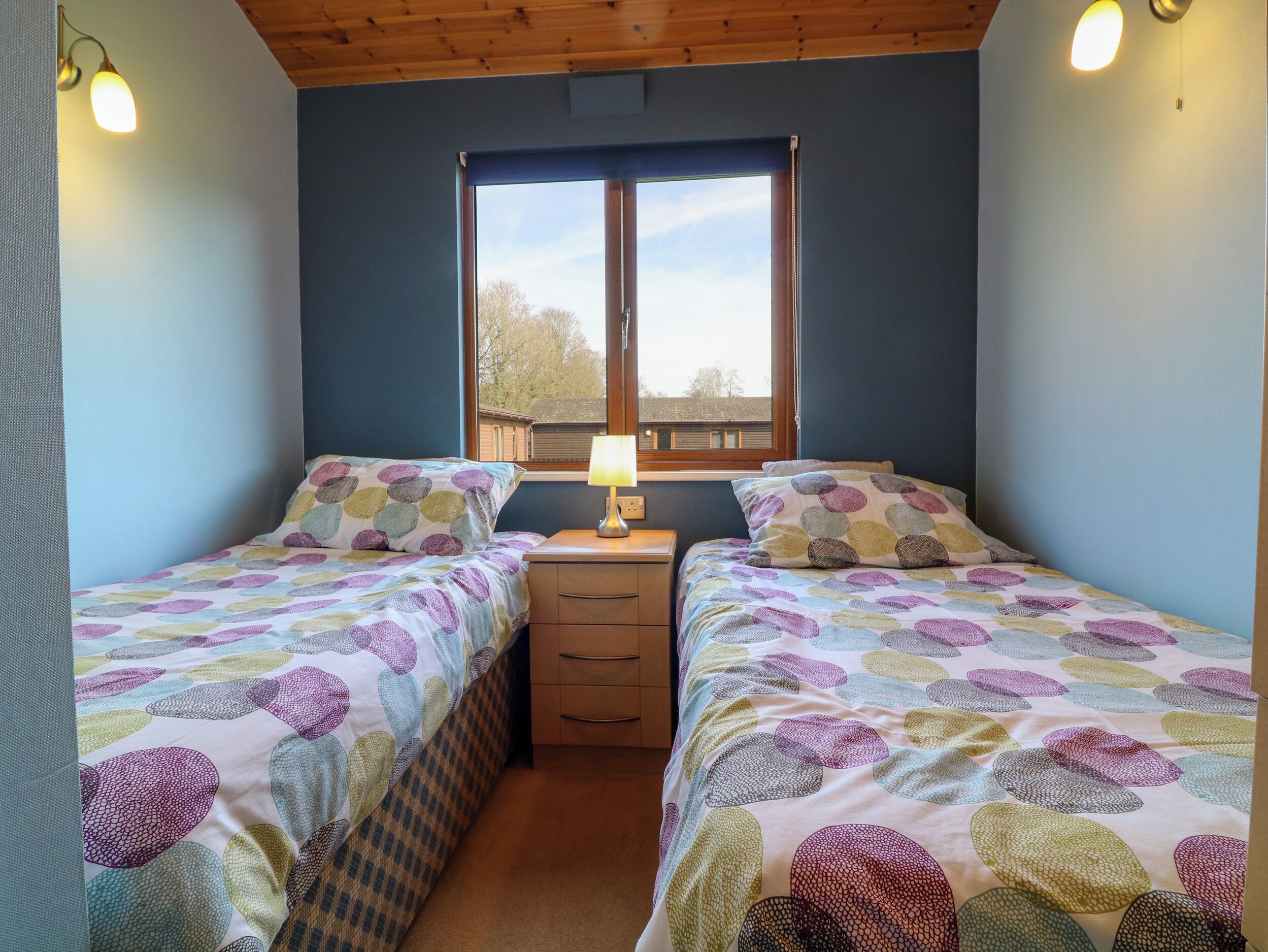 A bedroom with two beds, a window, and a nightstand with a lamp.