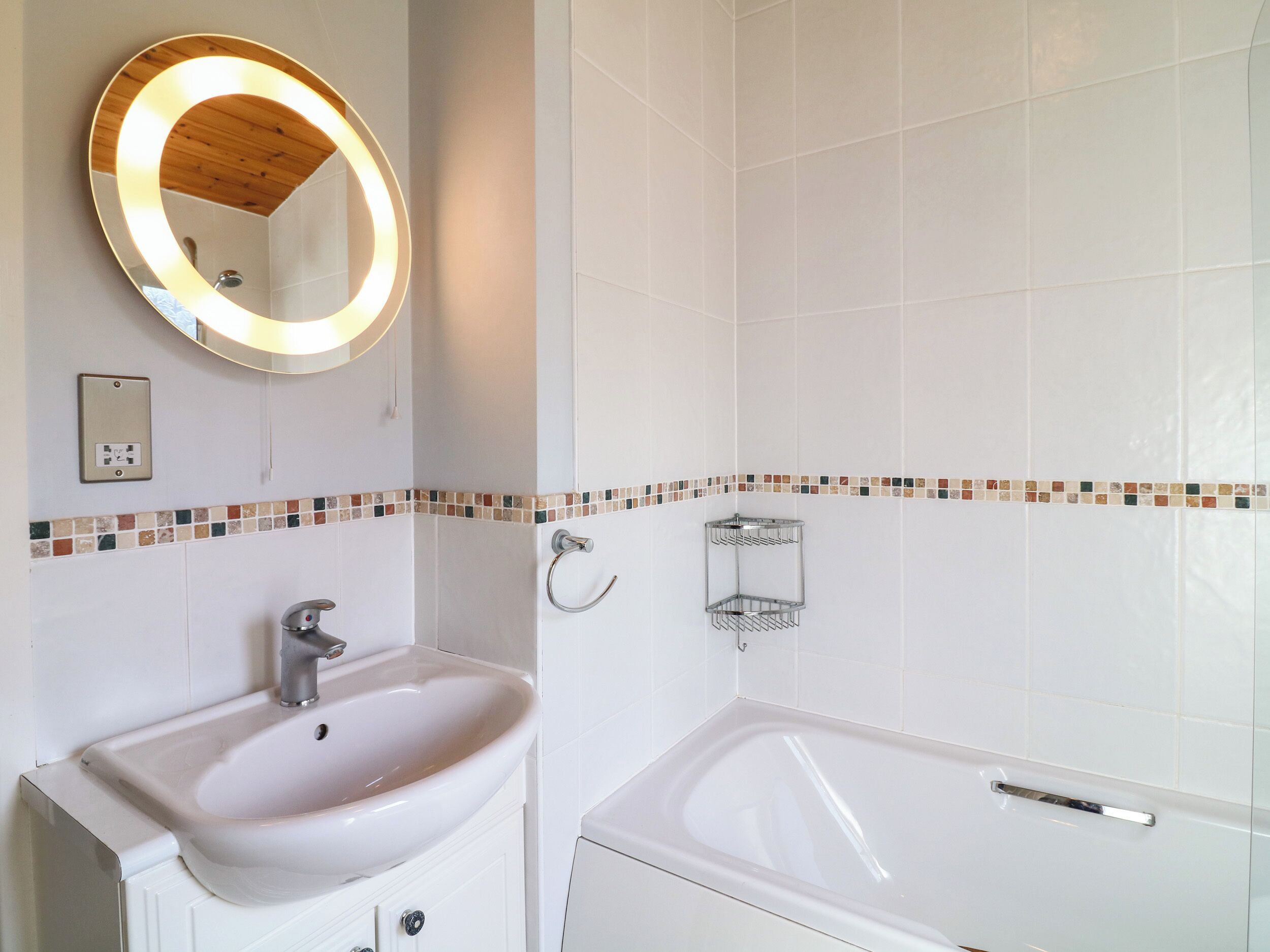 Une salle de bain avec un lavabo blanc, un miroir avec un cadre en bois et une baignoire.