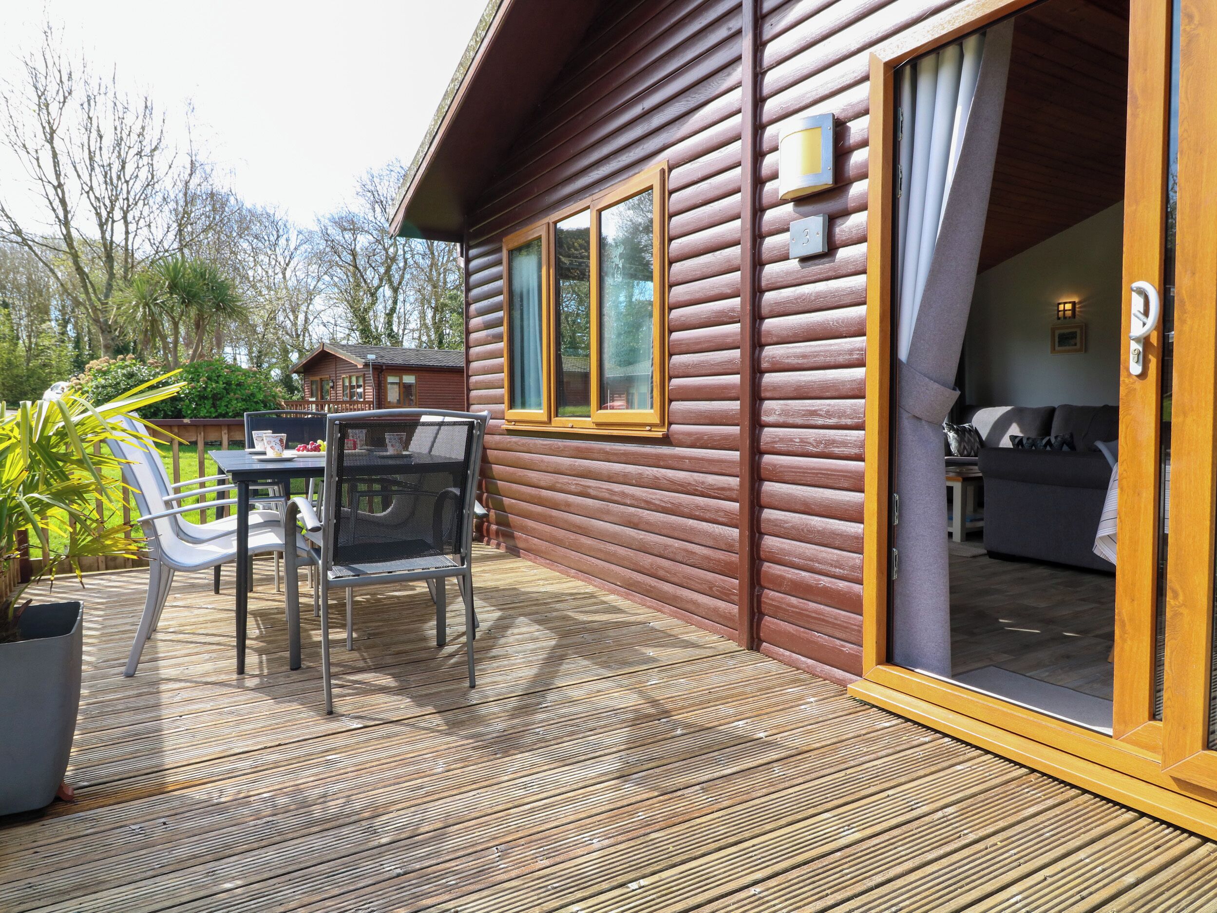 A wooden cabin with a deck, a dining table with chairs, and a sofa inside.