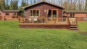 A wooden cabin with a deck, large windows, and a small outdoor seating area.