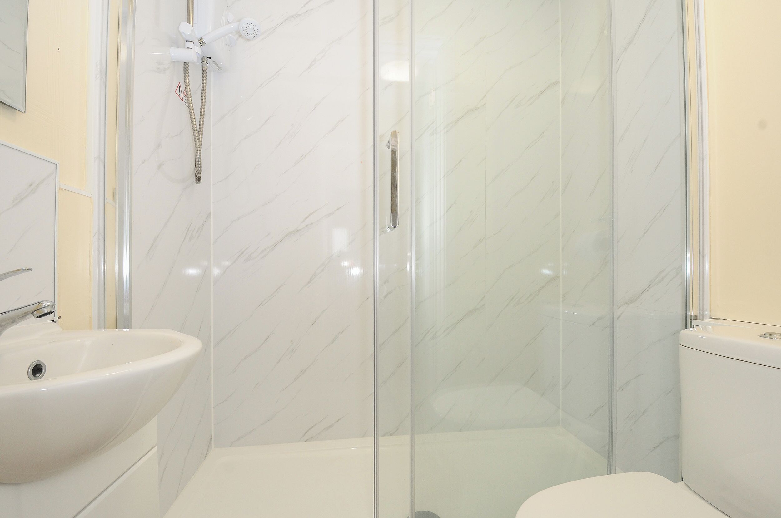 Une salle de bain avec une douche à parois de verre, un lavabo blanc et des toilettes.