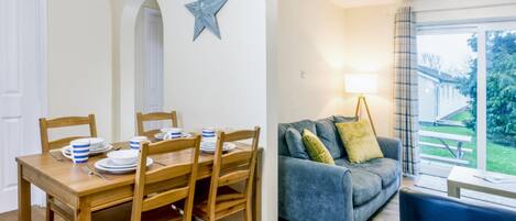 A dining area with a wooden table and chairs, a blue star decoration on the wall, and a grey sofa with cushions.