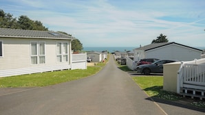 A row of mobile homes with a paved road in between, a clear sky, and a view of the ocean in the distance.