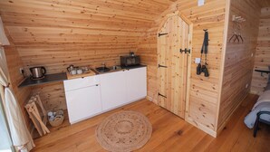 En liten, kompakt trästuga med ett minikök, en vävd matta och en säng med en sänggavel.
