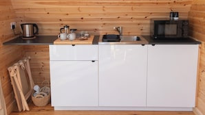 Ett kompakt kök med träpanel på väggarna, en vattenkokare i rostfritt stål, en mikrovågsugn, en diskho och en liten arbetsbänk med koppar och en skärbräda.