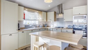 Una cocina moderna con armarios blancos, una isla central con taburetes, electrodomésticos de acero inoxidable y una ventana con persianas.