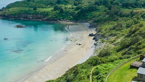 A coastal landscape with a beach, greenery, and a small building with a pathway leading to it. - Lodge 9 at Landscove Holiday Park (Brixham)