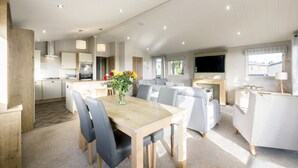 A spacious living area with a dining table, sofas, and a TV. - Lodge 15 at Landscove Holiday Park (Brixham)
