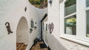 Ein schmaler Gang mit einer weißen Wand, einer Holztür und einem Fenster mit Blumenarrangements.