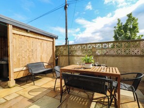An outdoor patio with a wooden table, four chairs, a potted plant, and a decorative fence. - 163 Manchester Road (Accrington)