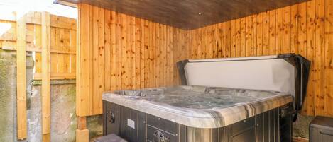 A hot tub with a wooden deck, a wooden wall, and a stone wall in the background.