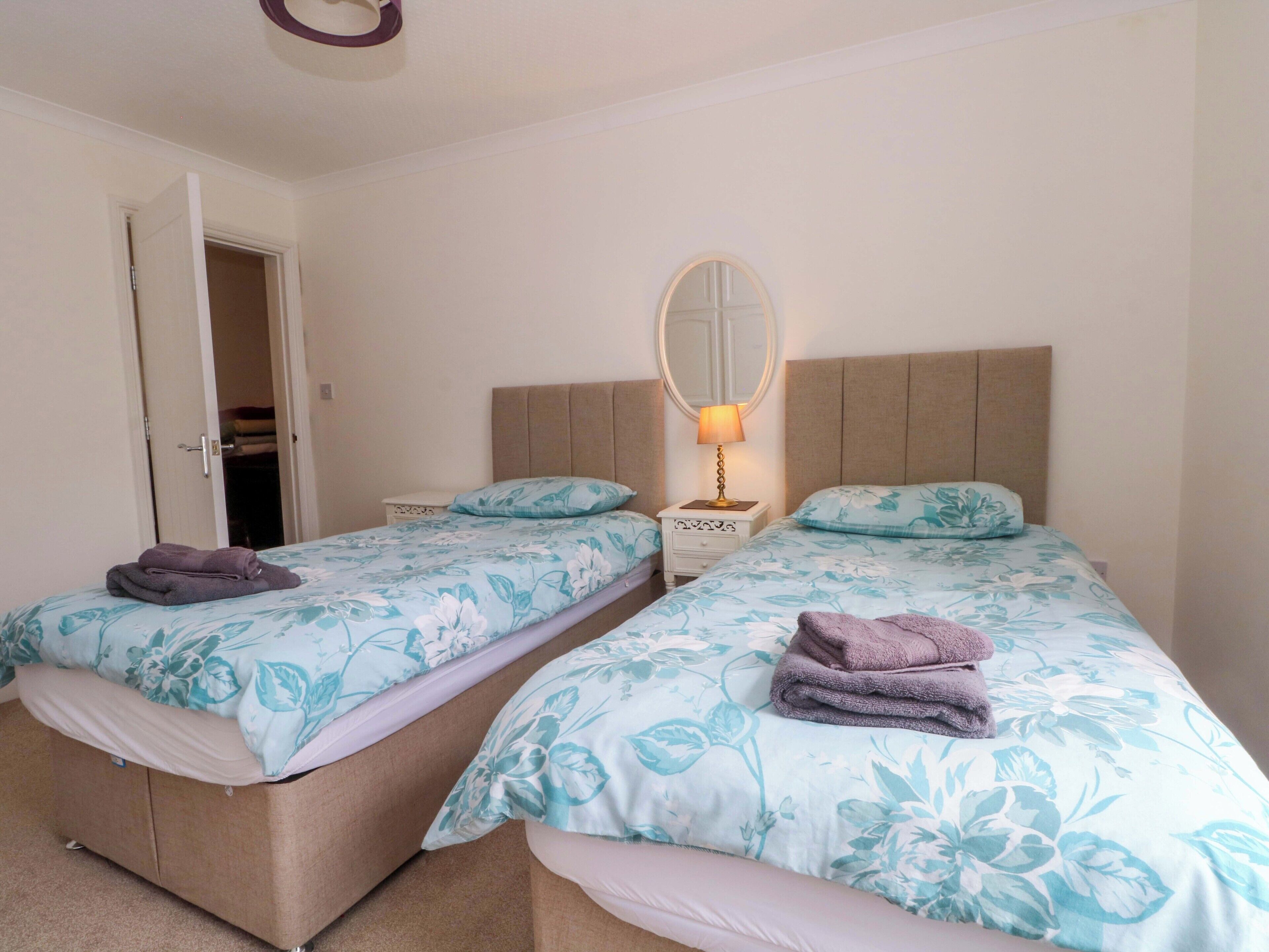 A hotel room with two beds, a bedside table with a lamp, a mirror, and a wardrobe.