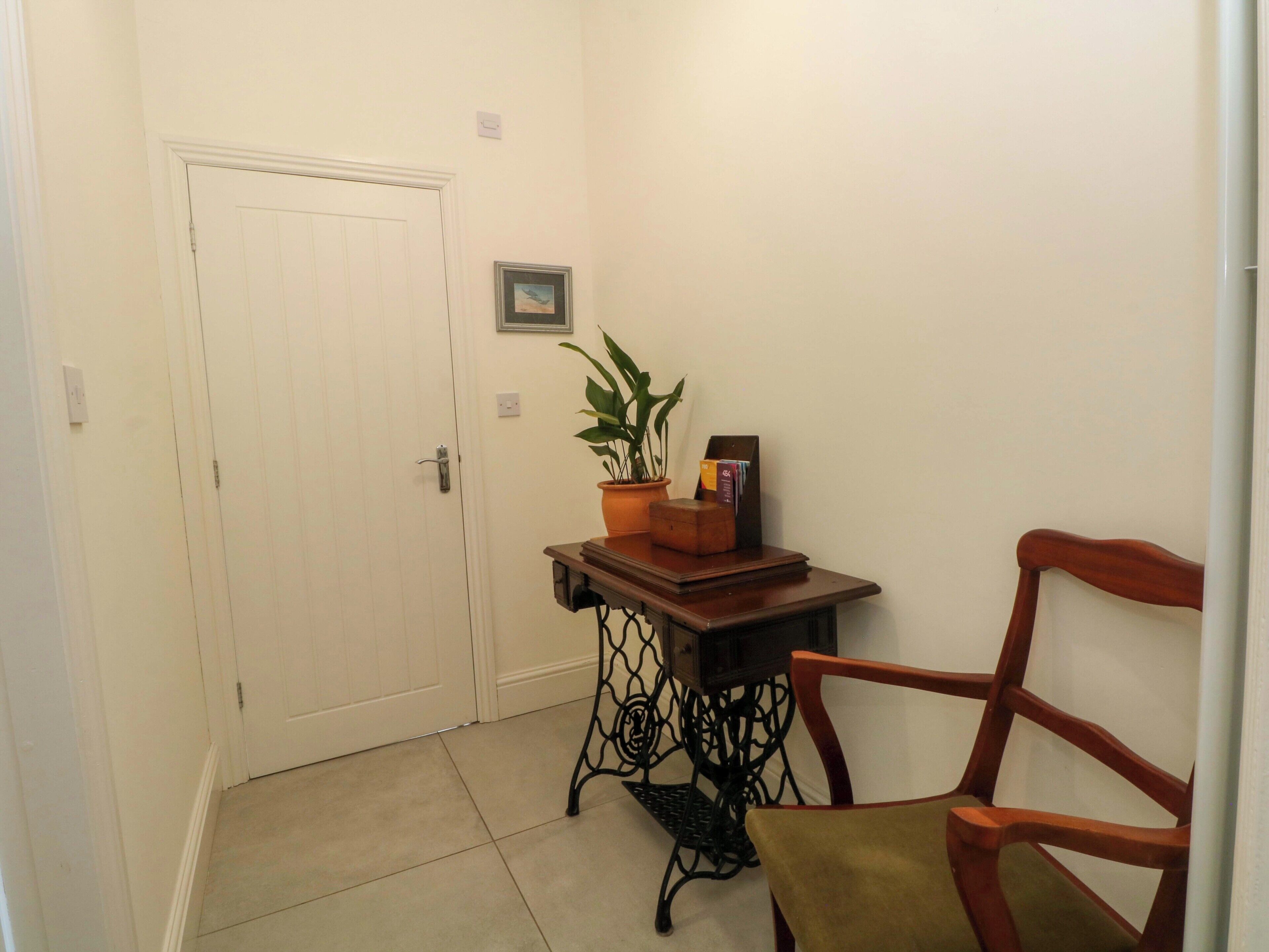 A hallway with a white door, a small table with a plant, a chair, and a framed picture on the wall.
