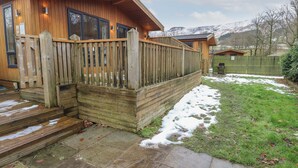 A wooden cabin with a wooden deck, stone steps, and a grassy yard with snow patches. - Dovestone Secluded Luxury Lodges - Pets Welcome (Oldham)