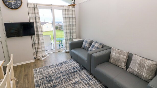 Ein modernes Wohnzimmer mit einem grauen Sofa, karierten Kissen, einem Flachbildfernseher und einem gemusterten Teppich.