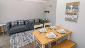 Ein modernes Wohnzimmer mit einem grauen Sofa, einem Holzesstisch gedeckt mit Tellern und Gläsern, und einem blau gemusterten Teppich.