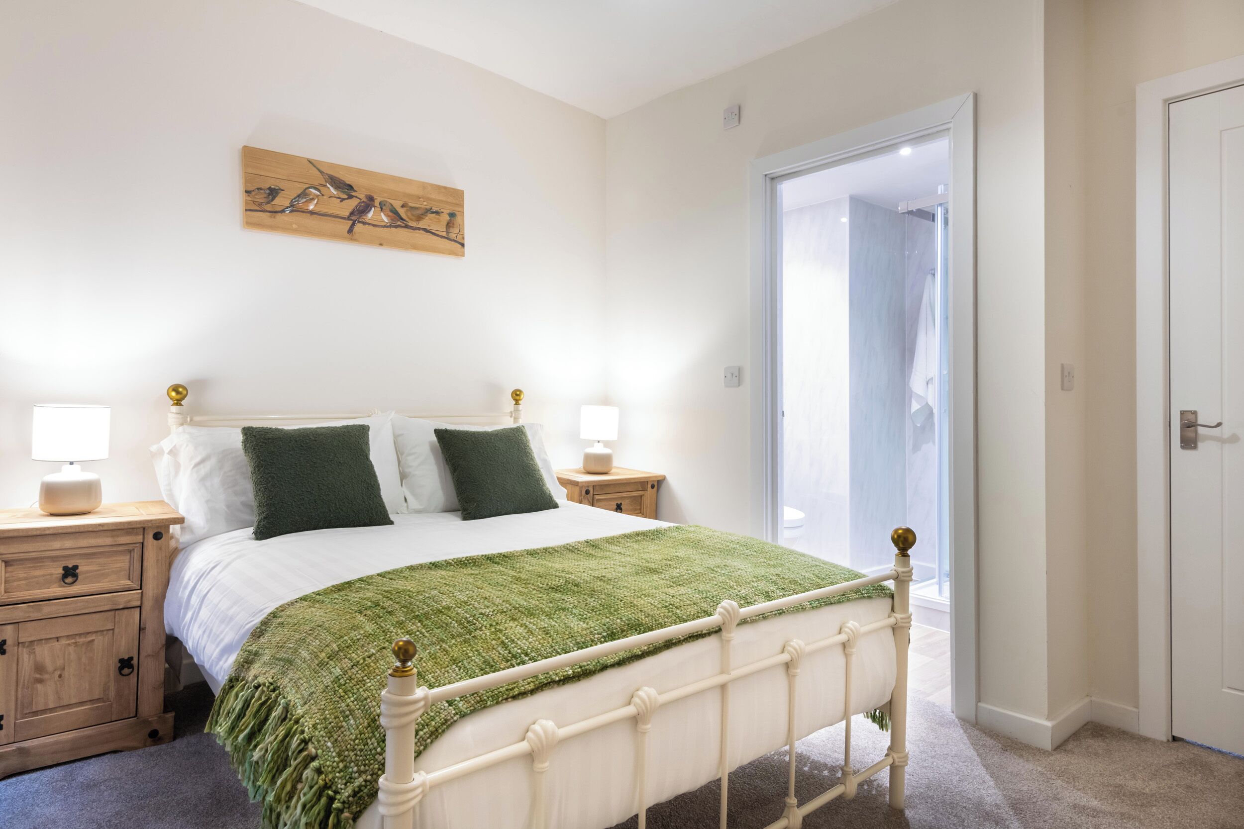 A bedroom with a bed, nightstands, a green throw blanket, and a wooden artwork on the wall.