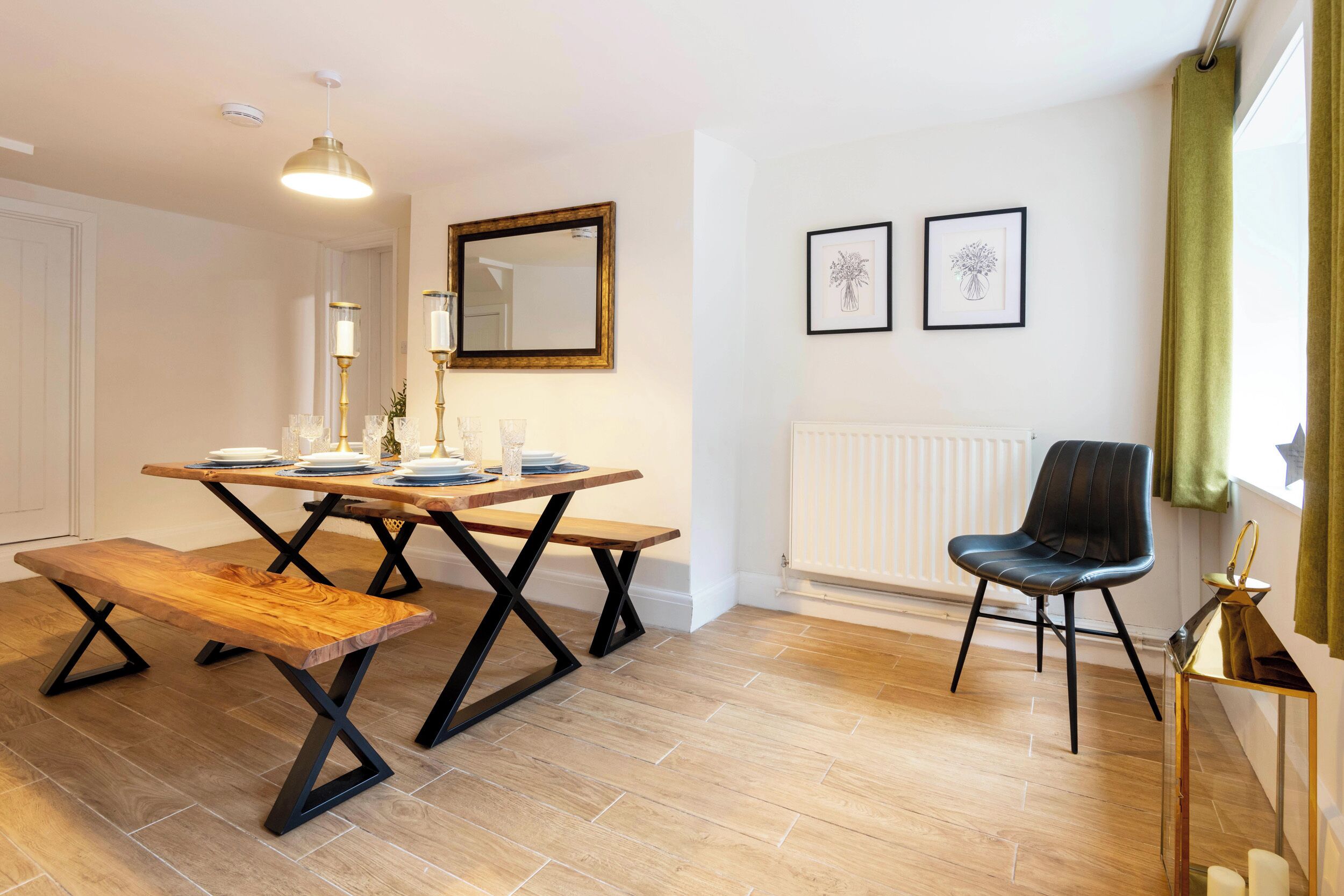 A dining area with a wooden table and benches, a black chair, a pendant light, and two framed pictures on the wall.