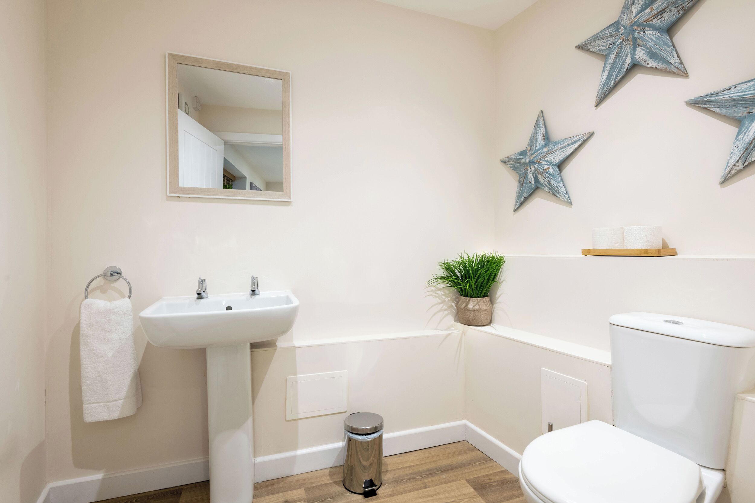 Een badkamer met een witte wastafel, toilet en een kleine prullenbak. Boven de wastafel hangt een spiegel en aan de muur is een sterren decoratie.